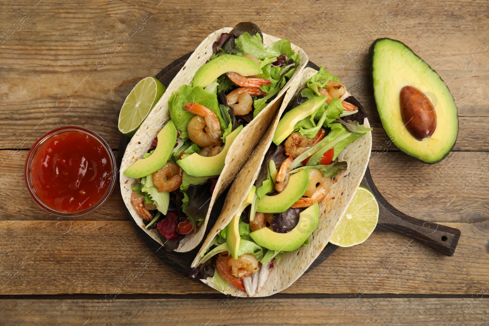 Photo of Delicious tacos with shrimps, avocado and sauce on wooden table, flat lay