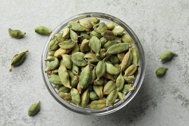 Photo of Glass bowl with dry cardamom pods on light grey table, top view