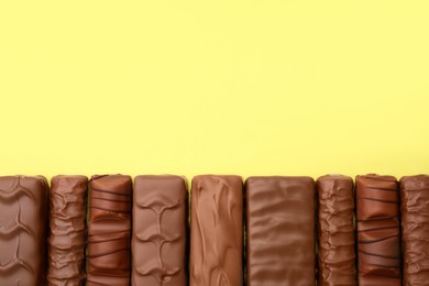 Different tasty chocolate bars on yellow background, flat lay. Space for text