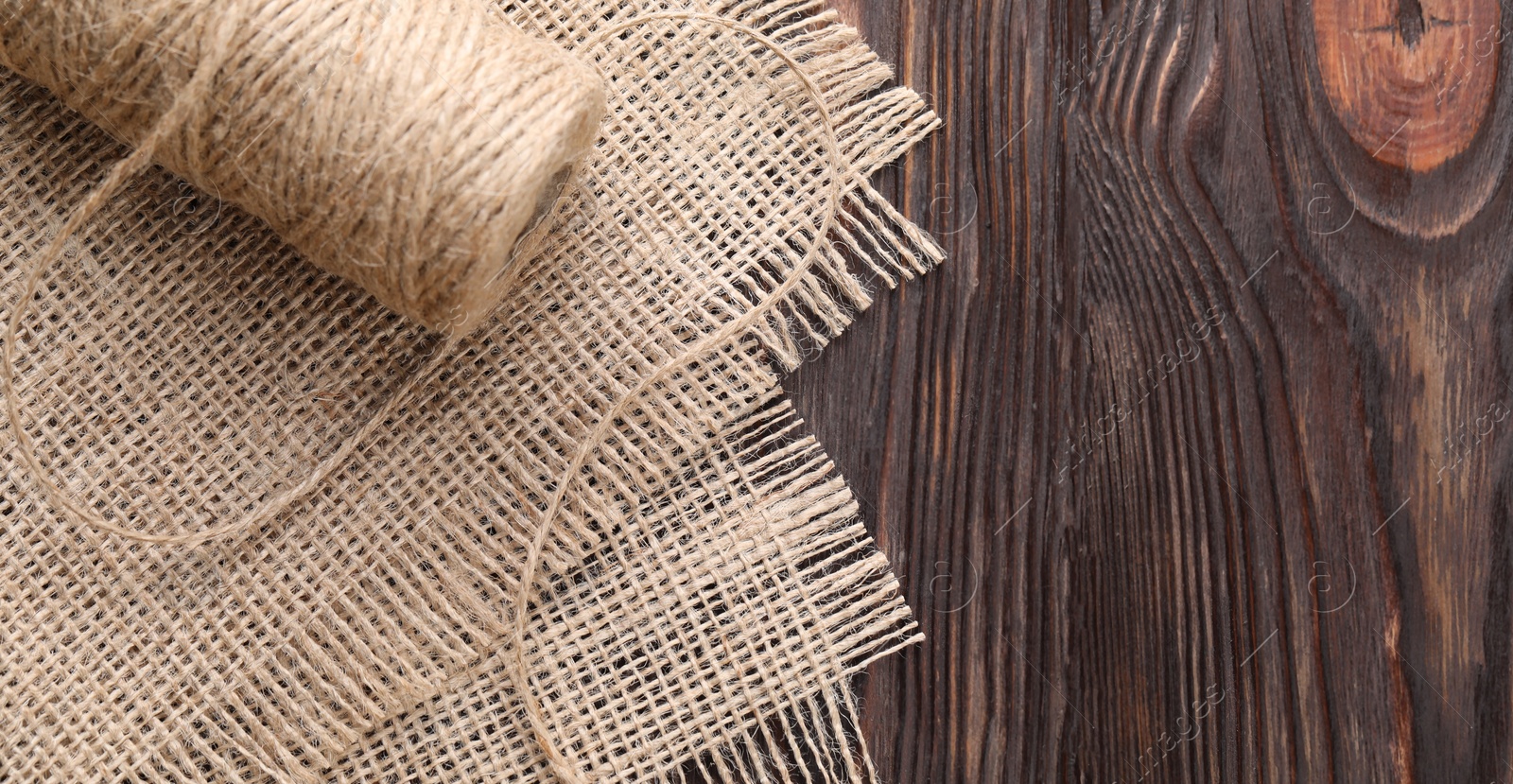 Photo of Spool of thread and burlap fabric on wooden table, top view. Space for text