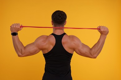 Photo of Young man exercising with elastic resistance band on orange background, back view