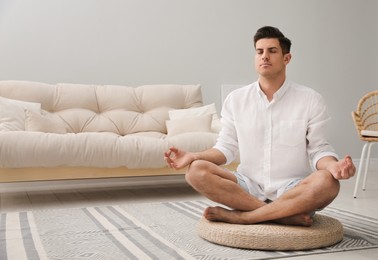 Photo of Man meditating on wicker mat at home. Space for text