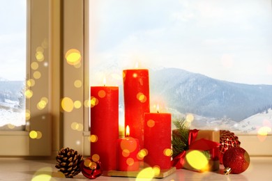 Image of Red burning candles, gift box and festive decor on window sill indoors. Christmas eve