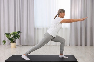Photo of Senior woman practicing yoga on mat at home