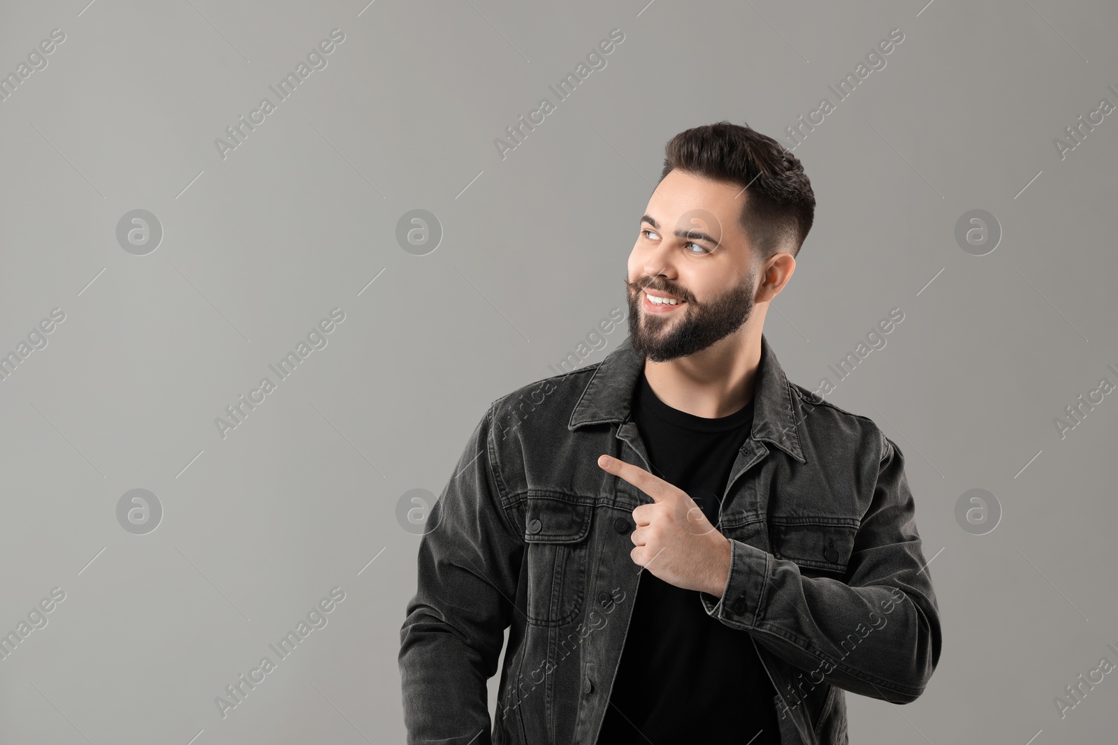 Photo of Young man with mustache pointing at something on grey background. Space for text
