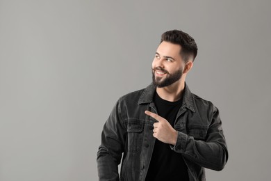 Young man with mustache pointing at something on grey background. Space for text