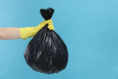 Photo of Woman holding plastic bag full of garbage on light blue background, closeup. Space for text