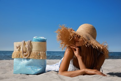 Photo of Woman with beach bag and straw hat lying on sand near sea