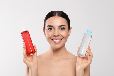 Young woman with bottles of micellar water on light grey background