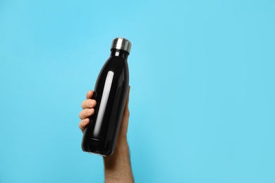 Photo of Man holding black thermos bottle on light blue background, closeup. Space for text