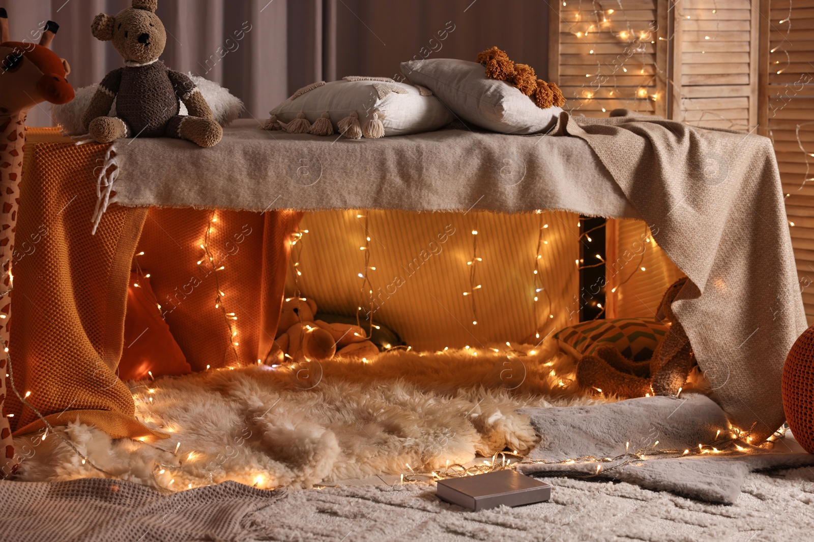 Photo of Beautiful play tent decorated with festive lights and toys at home