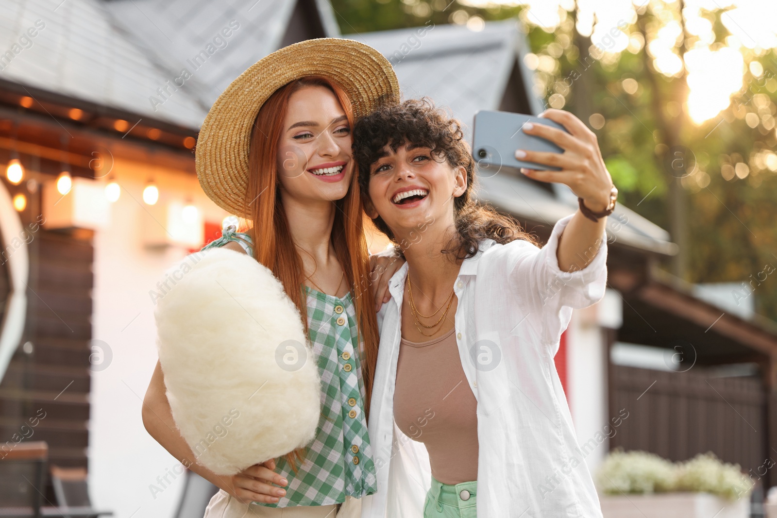 Photo of Happy friends with cotton candy taking selfie outdoors