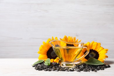 Sunflower cooking oil, seeds and yellow flowers on white wooden table, space for text