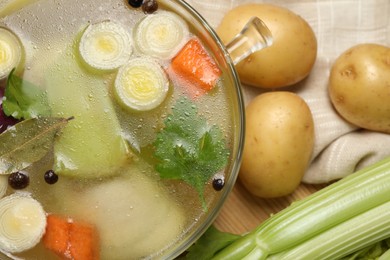 Photo of Glass pot with tasty bouillon and different ingredients on wooden table, flat lay