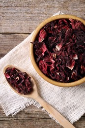 Photo of Bowl and spoon with dry hibiscus tea on wooden table, flat lay