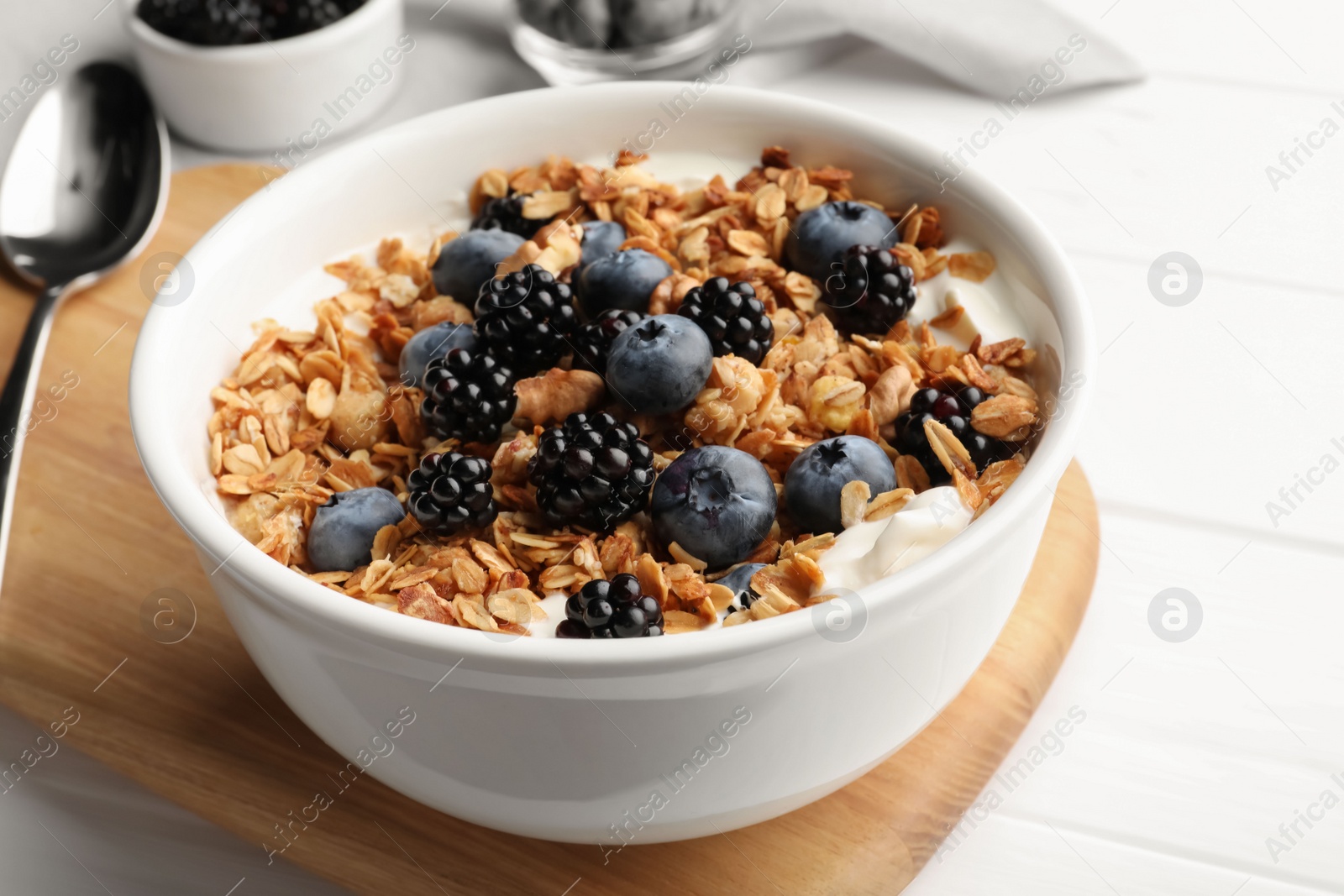 Photo of Bowl of healthy muesli served with berries on white wooden table, closeup