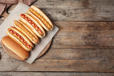 Photo of Tasty fresh hot dogs on wooden table, top view. Space for text