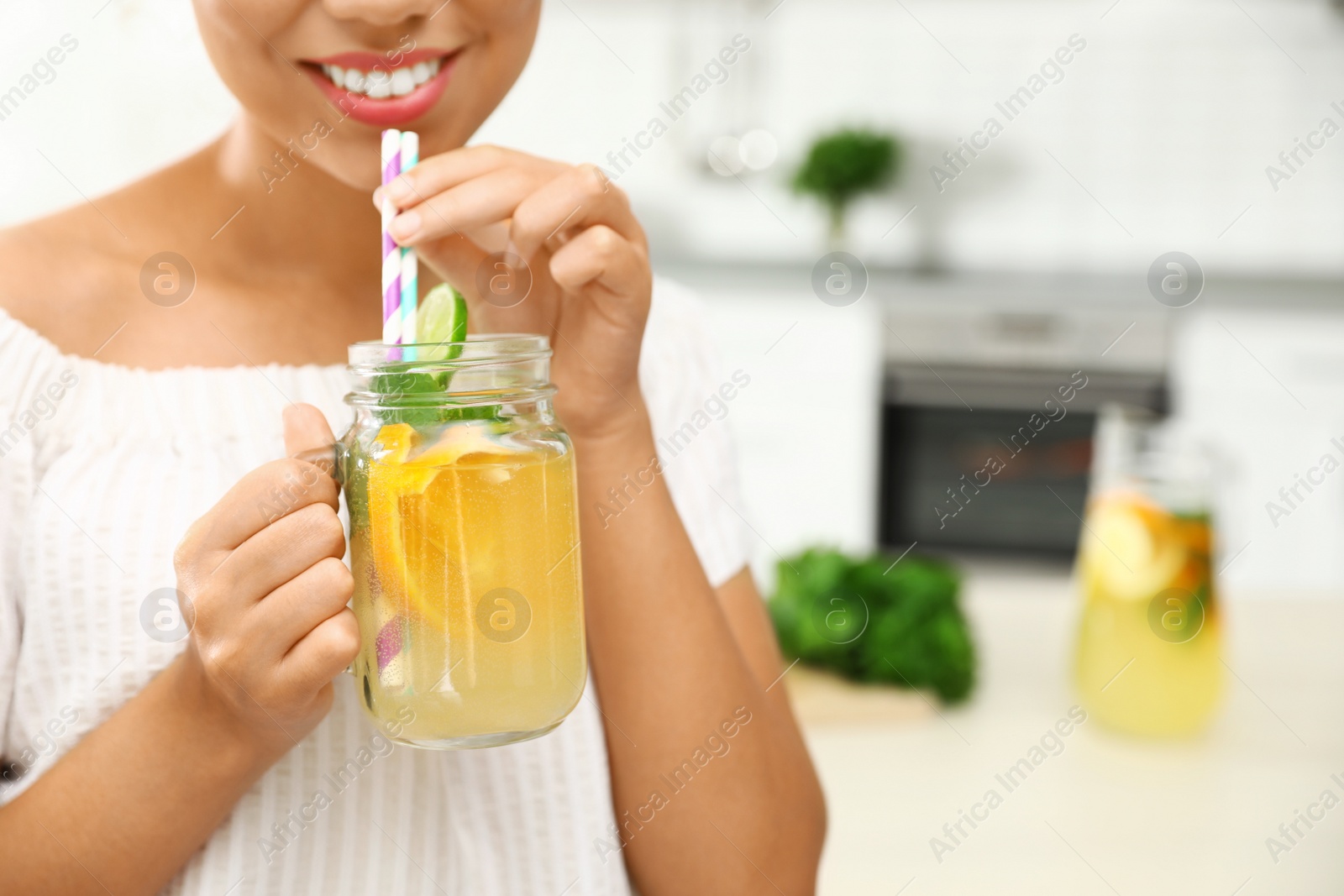 Photo of Happy African-American woman with mason jar of natural lemonade in kitchen, closeup. Detox drink