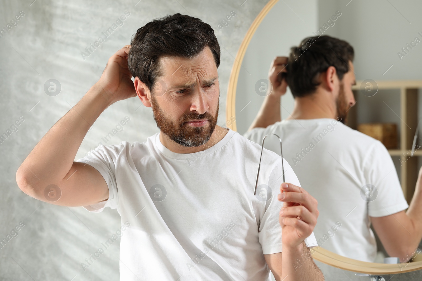 Photo of Confused man with tongue cleaner in bathroom