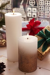 Beautiful burning candles with Christmas decor on white wooden table near window