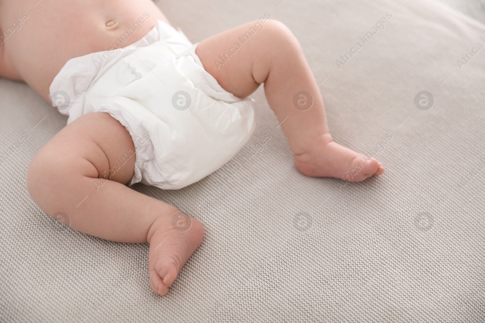 Photo of Cute little baby in diaper lying on bed, closeup