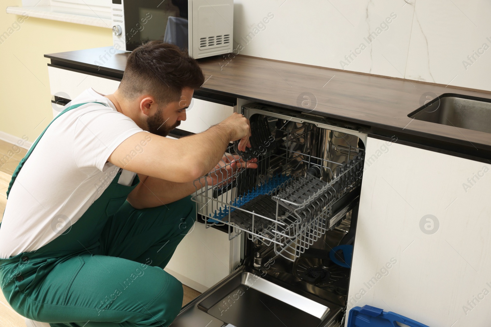 Photo of Serviceman examining dishwasher cutlery rack in kitchen