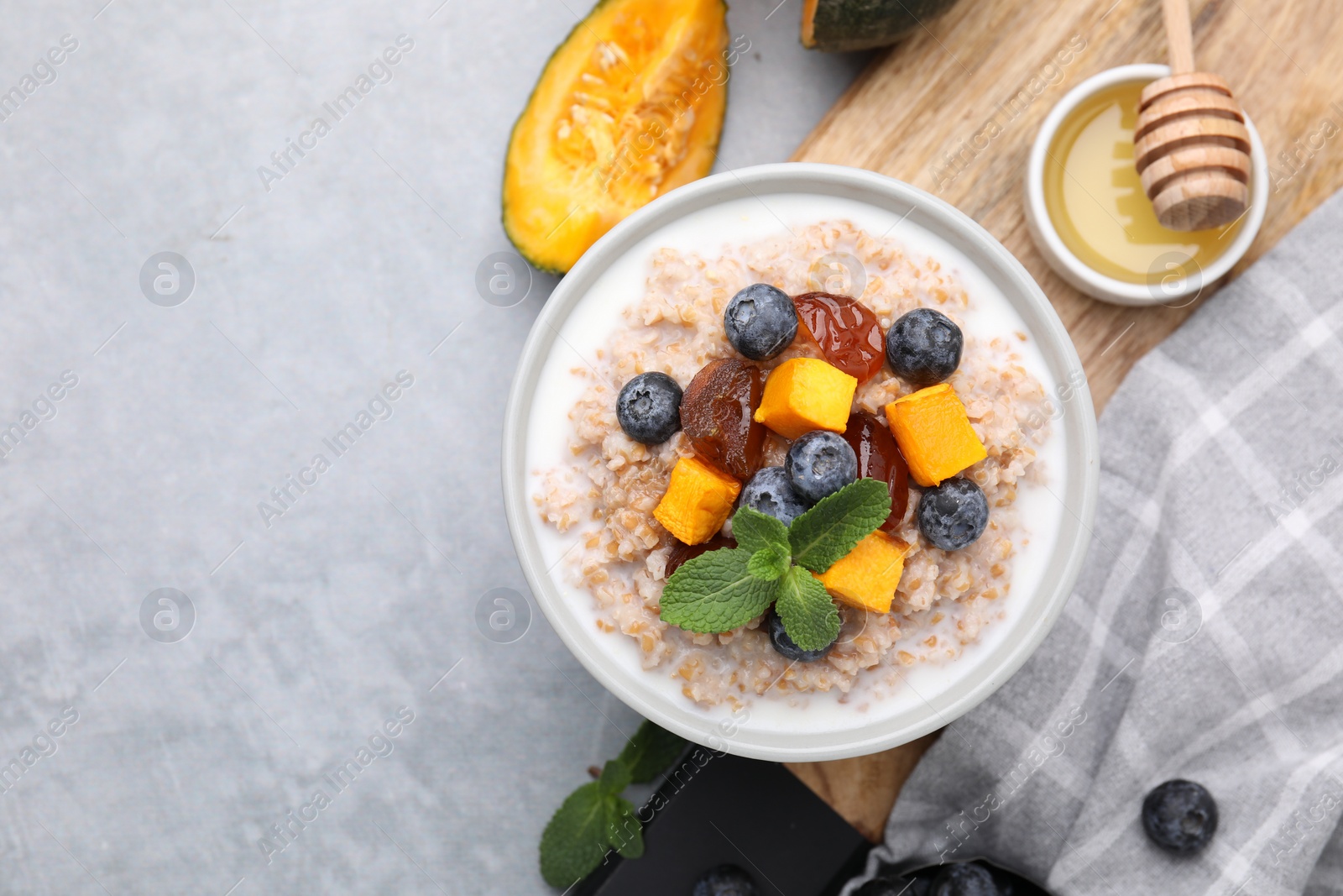 Photo of Tasty wheat porridge with pumpkin, dates and blueberries in bowl on light gray table, flat lay. Space for text