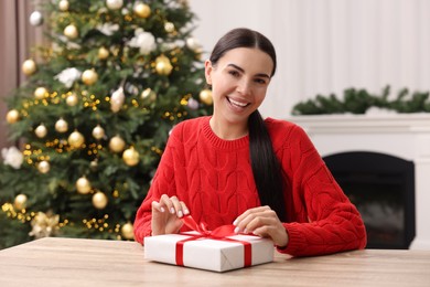 Photo of Happy woman opening Christmas gift at wooden table in room