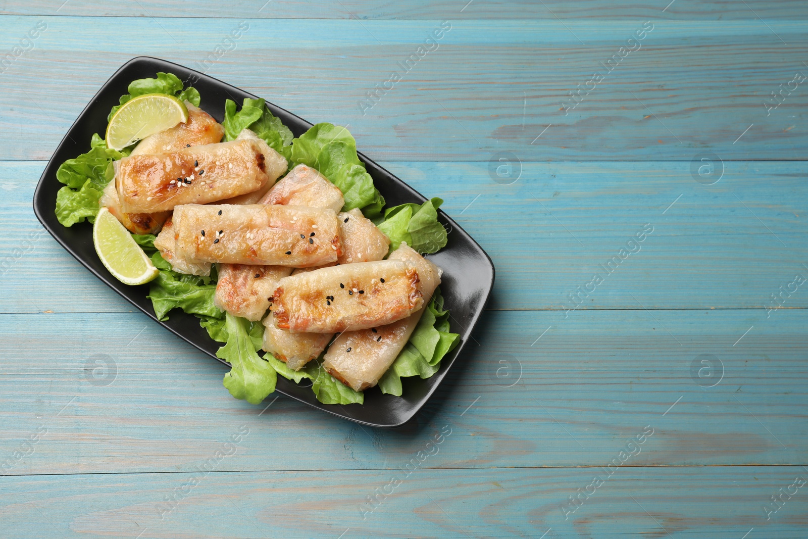 Photo of Tasty fried spring rolls, lettuce and lime on light blue wooden table, top view. Space for text