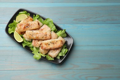 Photo of Tasty fried spring rolls, lettuce and lime on light blue wooden table, top view. Space for text