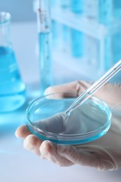 Scientist dripping liquid from pipette into petri dish in laboratory, closeup