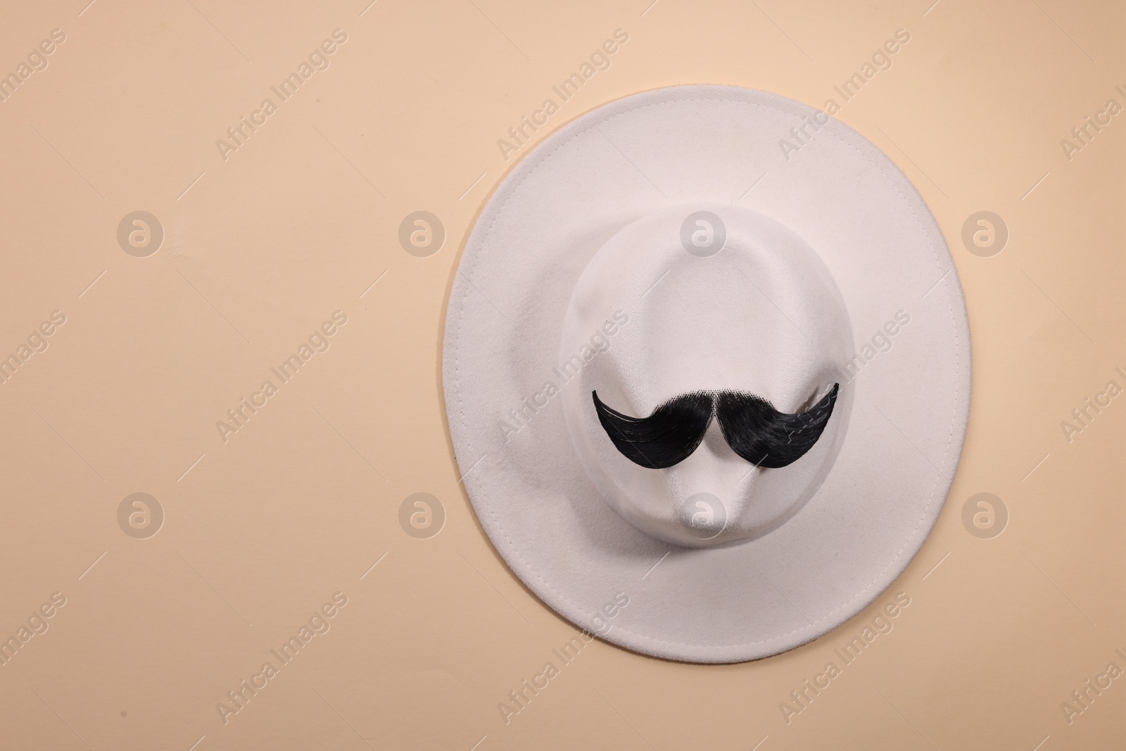 Photo of Man's face made of artificial mustache and hat on beige background, top view. Space for text