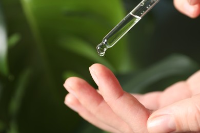 Photo of Woman applying cosmetic serum onto finger on blurred background, closeup. Space for text