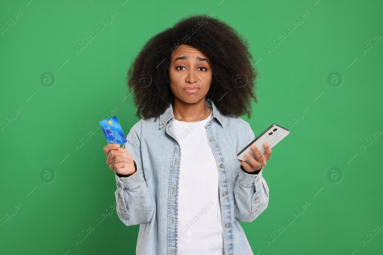 Photo of Confused woman with credit card and smartphone on green background. Debt problem