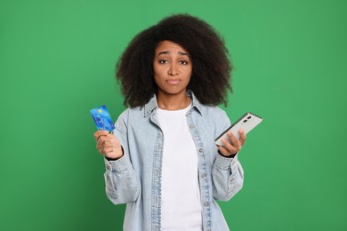 Photo of Confused woman with credit card and smartphone on green background. Debt problem