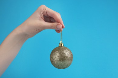 Woman holding glitter Christmas ball on light blue background, closeup