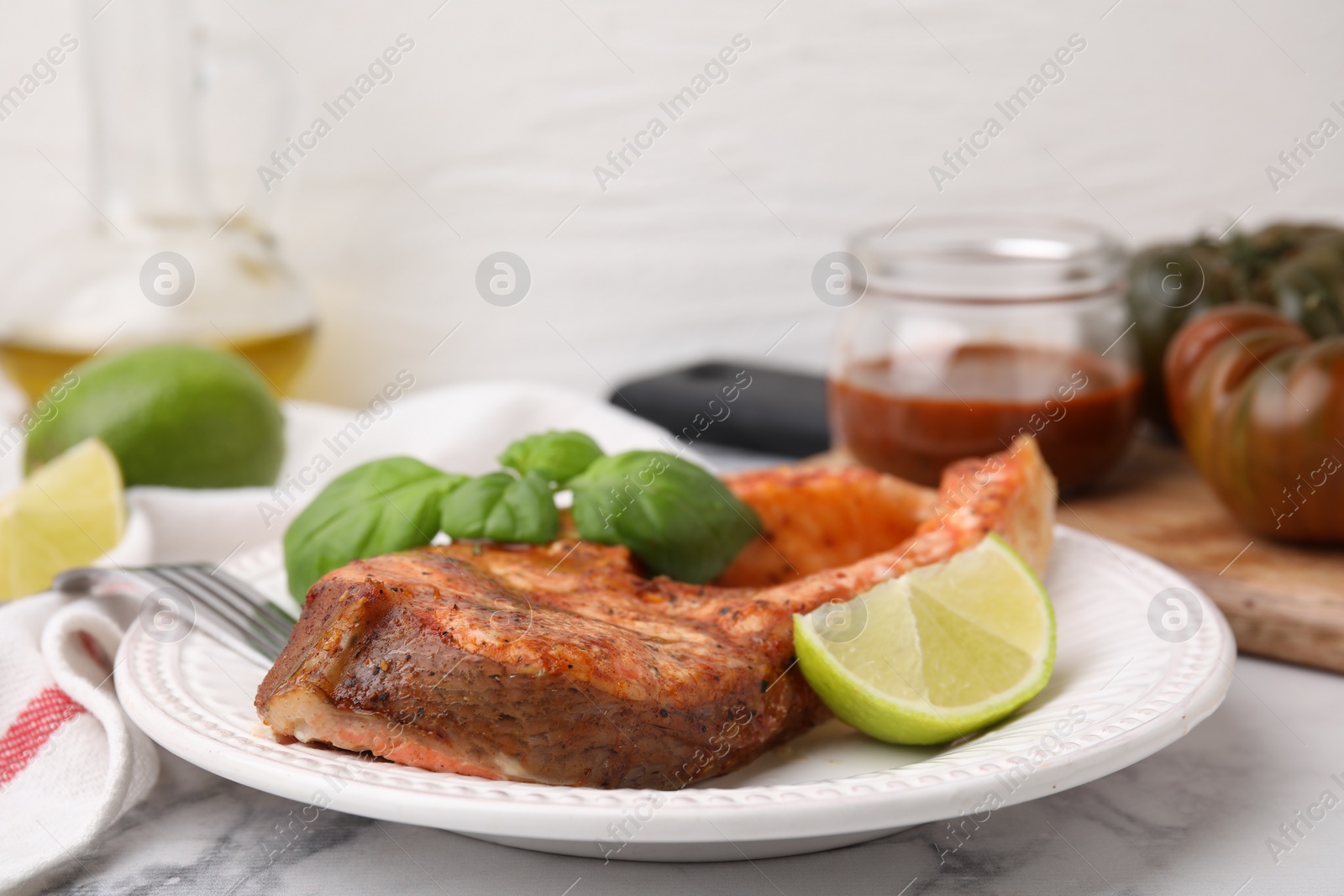 Photo of Freshly cooked fish, lime and basil on white marble table, closeup