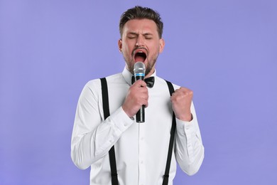 Photo of Handsome man with microphone singing on violet background