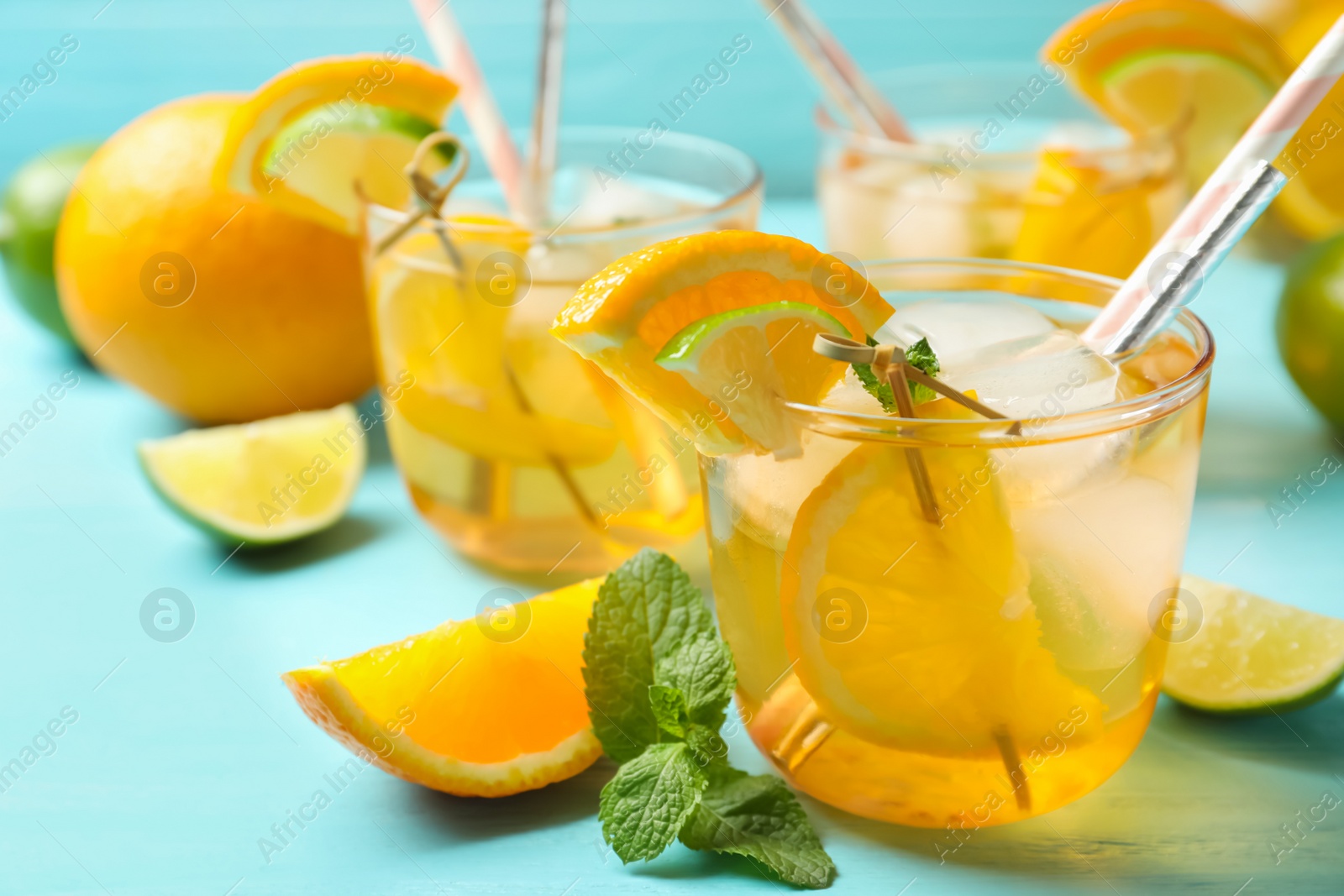 Photo of Delicious refreshing drink with orange and lime slices on light blue table, closeup