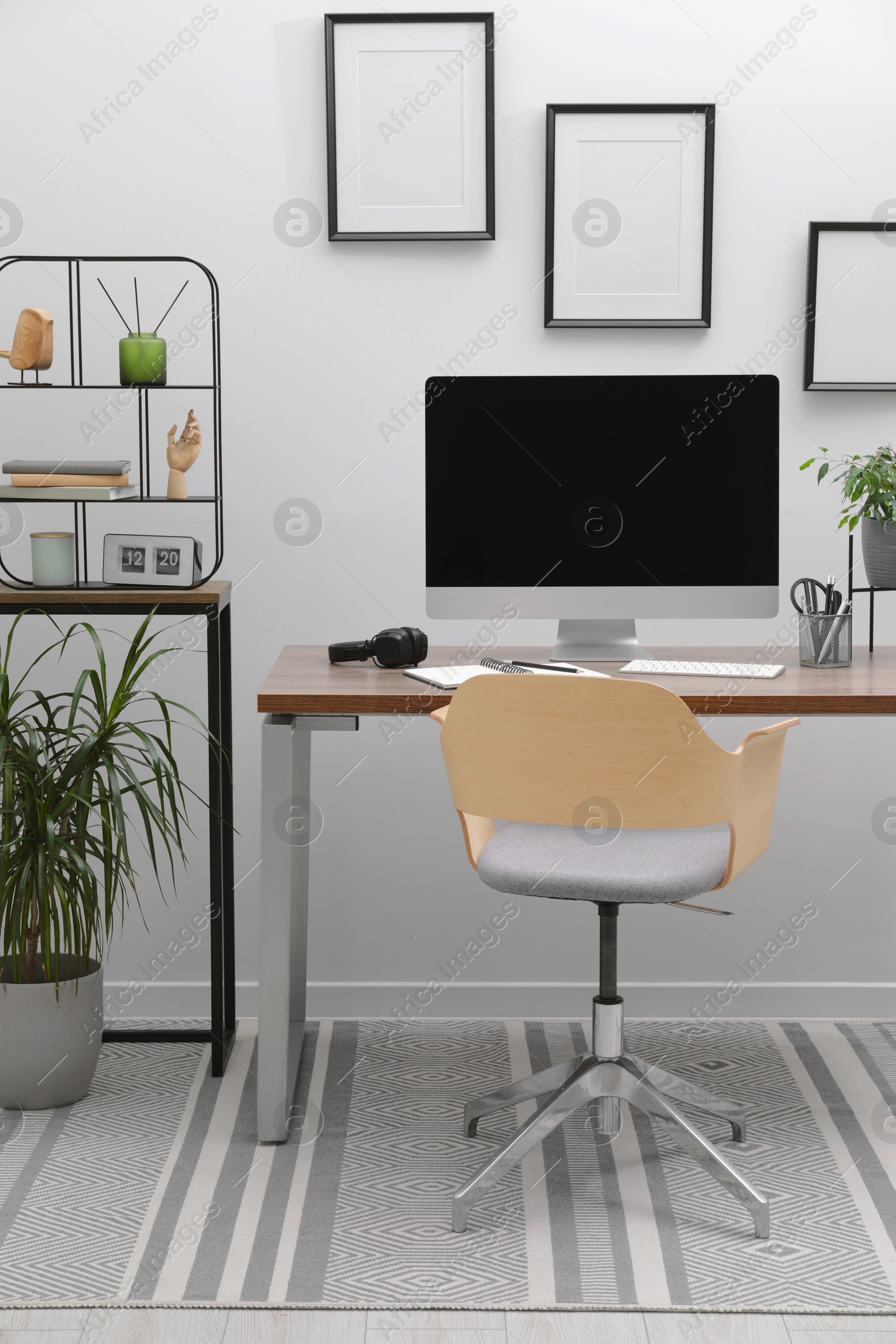 Photo of Cozy workspace with computer on desk, chair and houseplants near white wall at home