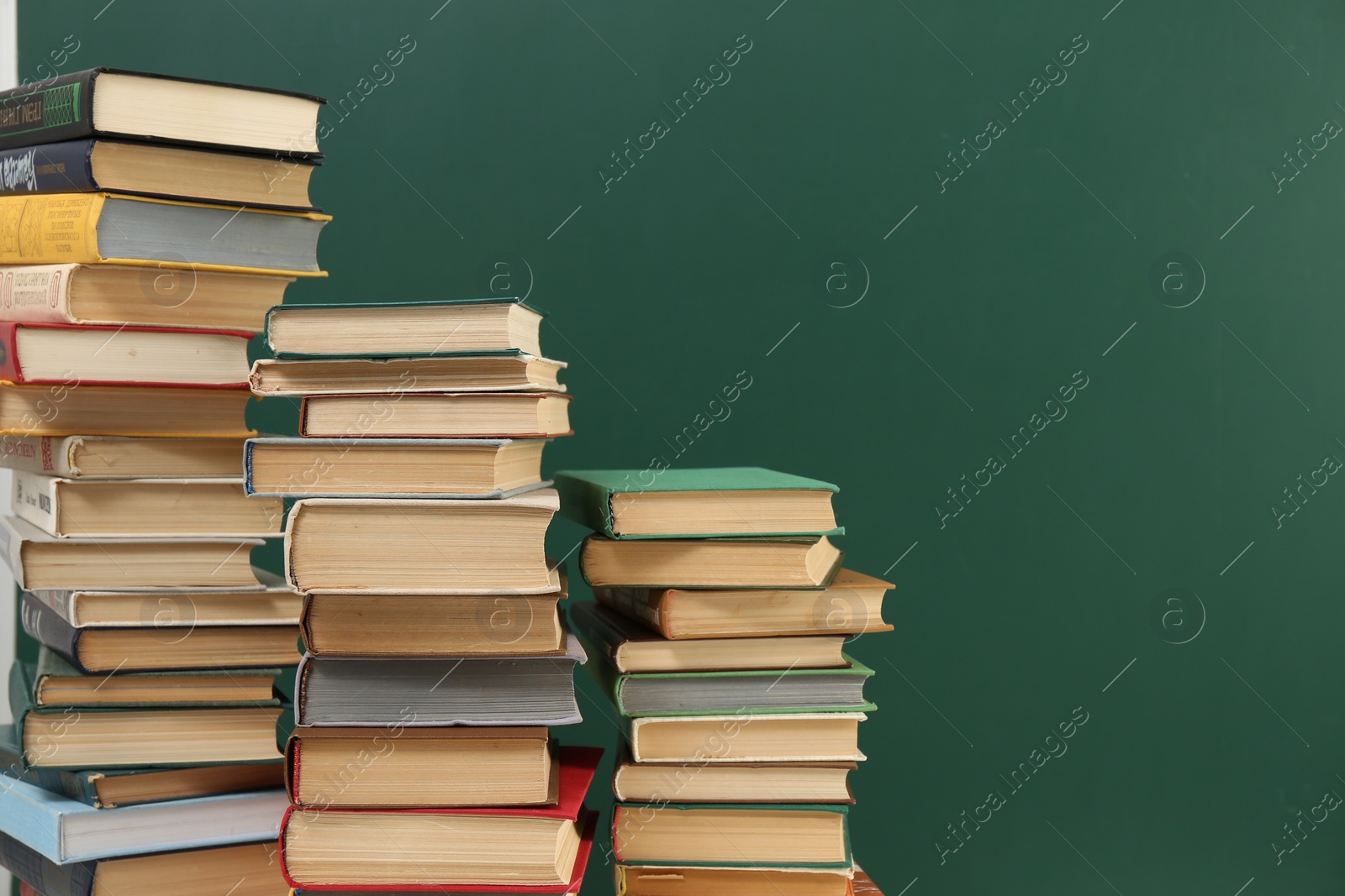 Photo of Many hardcover books near green chalkboard, space for text. Library material