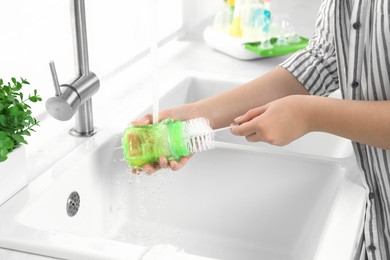 Photo of Woman washing baby bottle under stream of water in kitchen, closeup