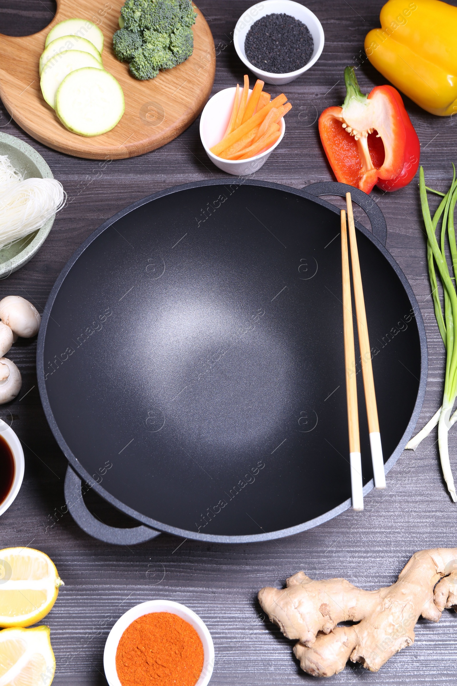 Photo of Empty iron wok, chopsticks and ingredients on dark grey wooden table, above view