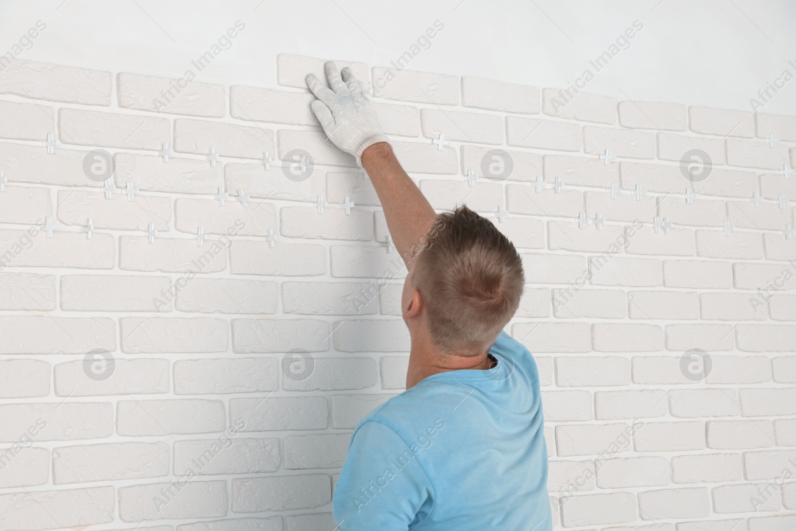 Photo of Professional builder installing new white decorative bricks on wall, back view