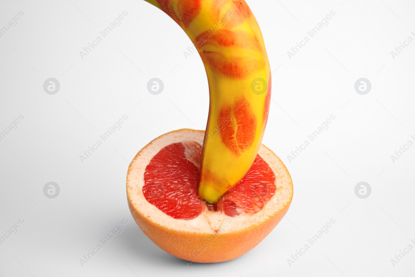 Photo of Fresh grapefruit and banana with red lipstick marks on white background. Sex concept