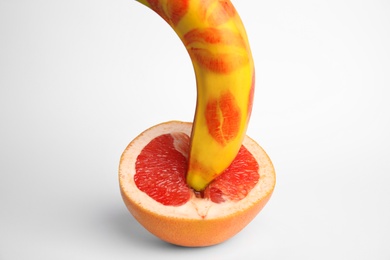 Photo of Fresh grapefruit and banana with red lipstick marks on white background. Sex concept