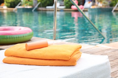 Photo of Beach towels and sunscreen on sun lounger near outdoor swimming pool, selective focus. Luxury resort