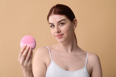 Photo of Washing face. Young woman with cleansing brush on beige background