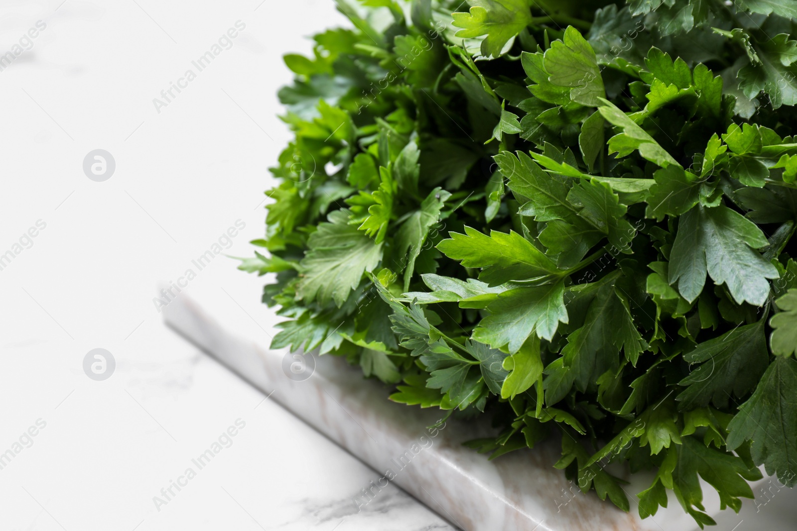 Photo of Bunch of fresh green parsley on white marble table, closeup