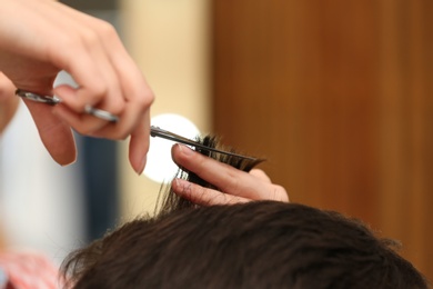 Barber making stylish haircut with professional scissors in beauty salon, closeup